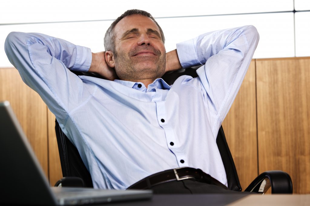 Businessman/real estate appraiser in blue shirt, smiling, with his hands behind his head as he leans back in an office chair, not worried about iBuyers.
